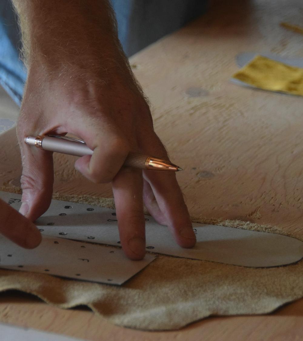 Manos trazan un patrón sobre una pieza de cuero en la mesa del taller