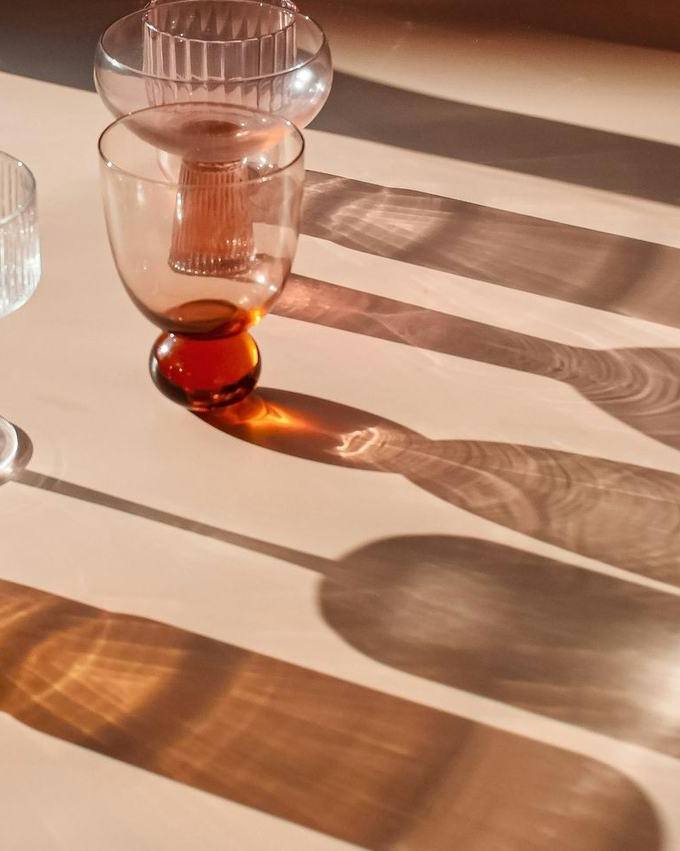 Vasos de vidrio con una bebida y sus sombras largas sobre una mesa clara