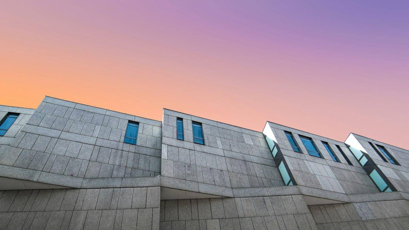 Edificio de hormigón con ventanas pequeñas bajo un cielo de atardecer violeta y naranja