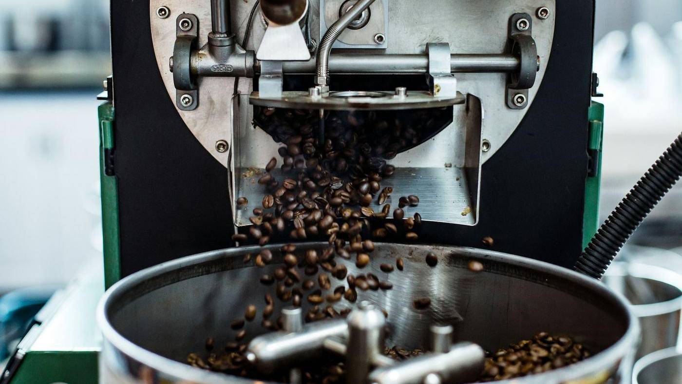 Granos de café cayendo desde una tostadora hacia el depósito de enfriado
