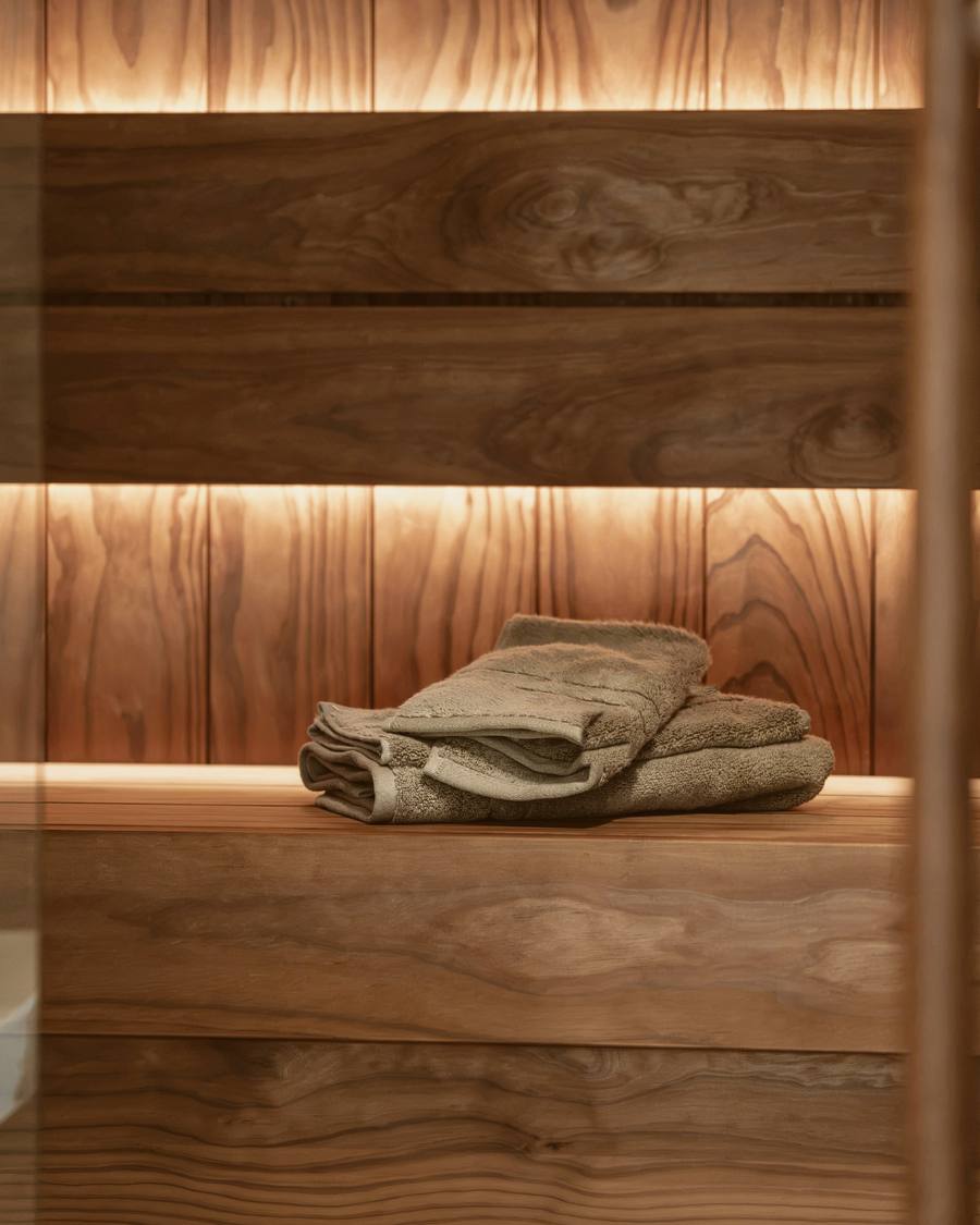 Toallas dobladas sobre un banco de sauna de madera, con una luz tenue tras los listones