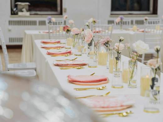 Una mesa larga puesta con flores rosadas y vajilla clara