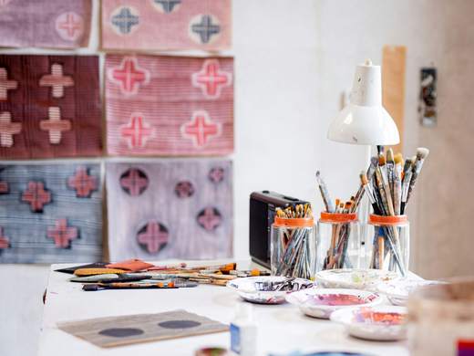 Mesa de taller con telas estampadas, pinceles y una lámpara