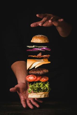 Ingredientes de una hamburguesa flotando entre dos manos