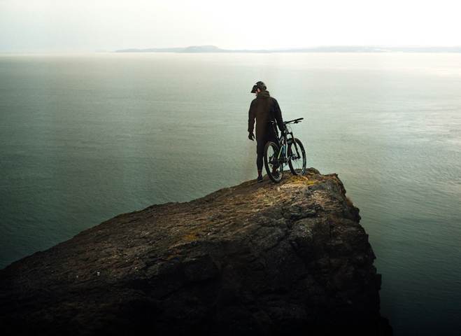 Ciclista de espaldas en lo alto de un acantilado frente al mar