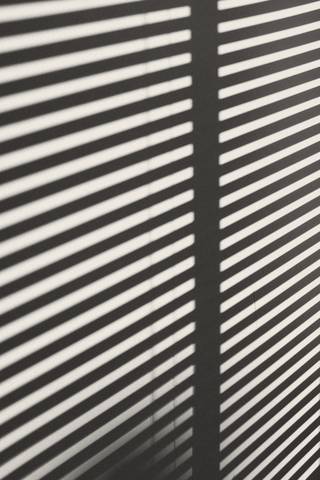 Franjas de luz y sombra de una persiana sobre un muro
