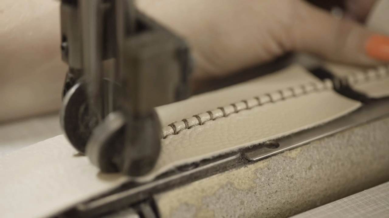 Una mano guía una tira de cuero bajo la aguja de una máquina de coser