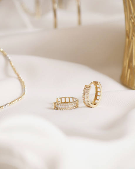Aros dorados con piedras claras sobre una tela color crema