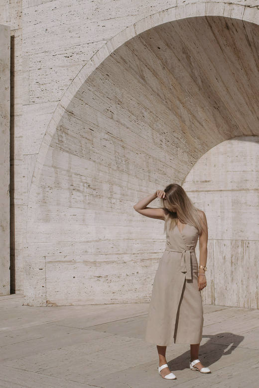 Vestido cruzado color arena bajo un arco de piedra, con el rostro oculto por el cabello
