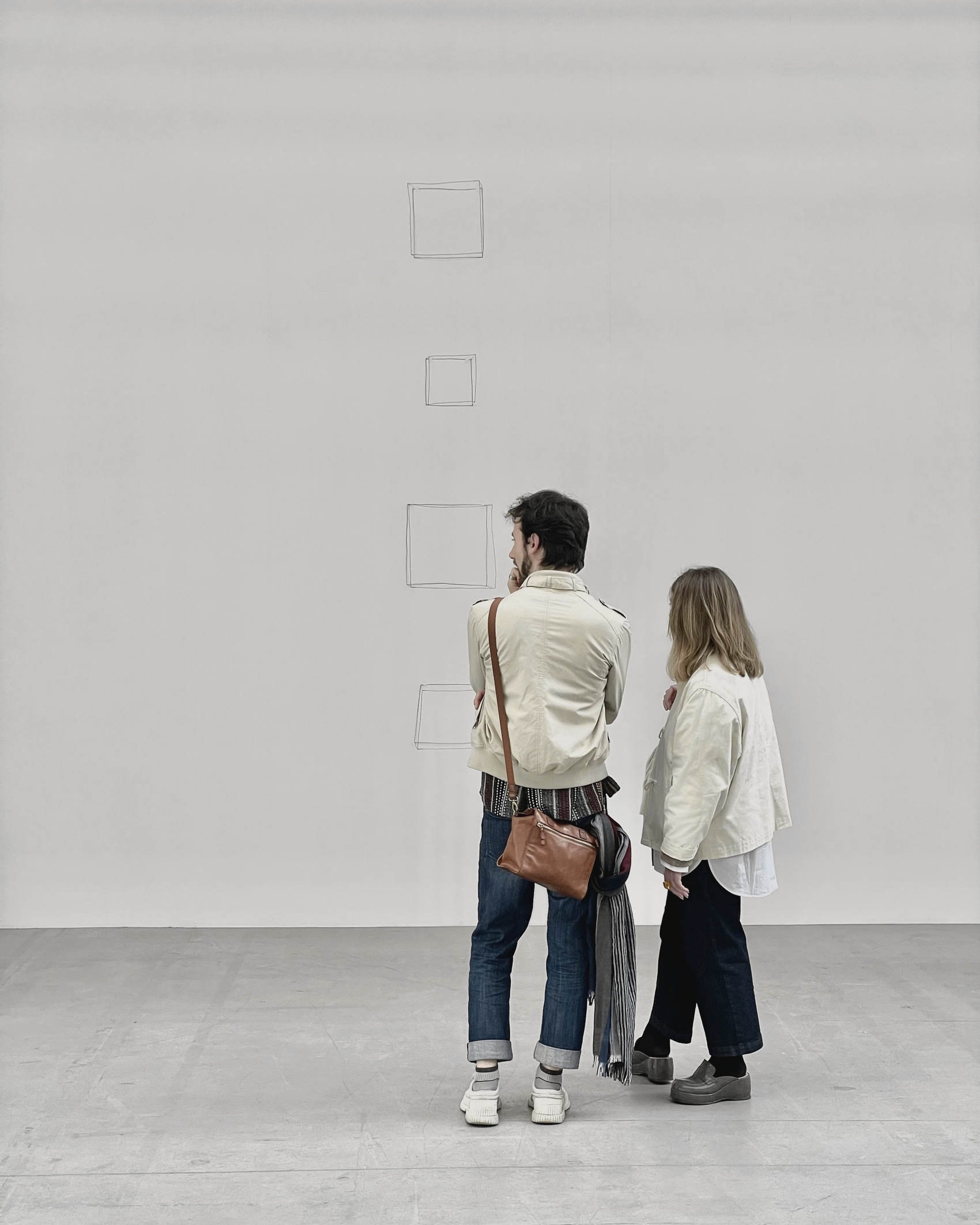 Dos personas de espaldas frente a una pared blanca de galería