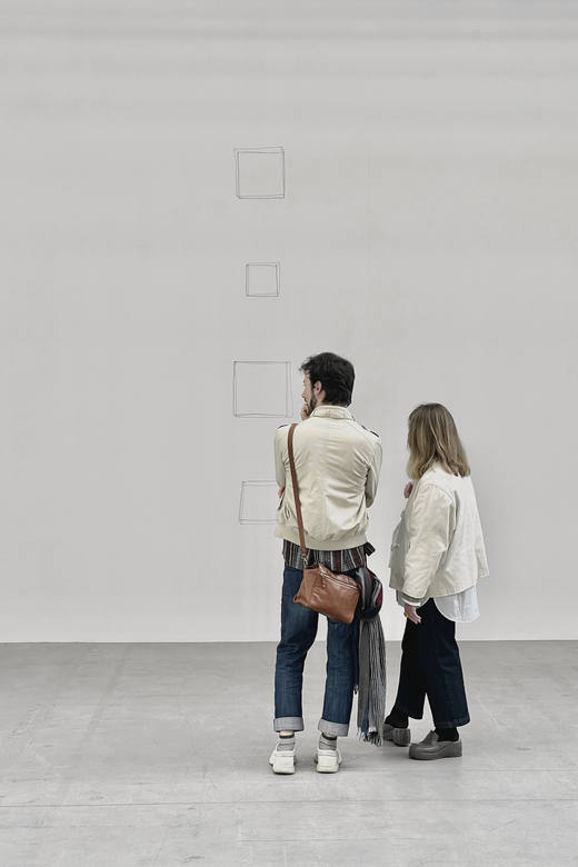 Dos personas de espaldas frente a una pared blanca de galería