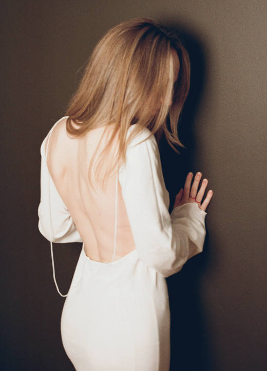 Espalda descubierta de un vestido blanco de manga larga, con el cabello cubriendo el rostro