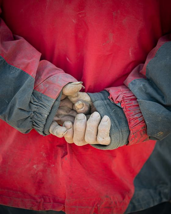Manos con guantes de trabajo, de espaldas, sobre una chaqueta roja
