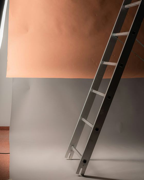 Una escalera de metal apoyada contra un fondo color durazno