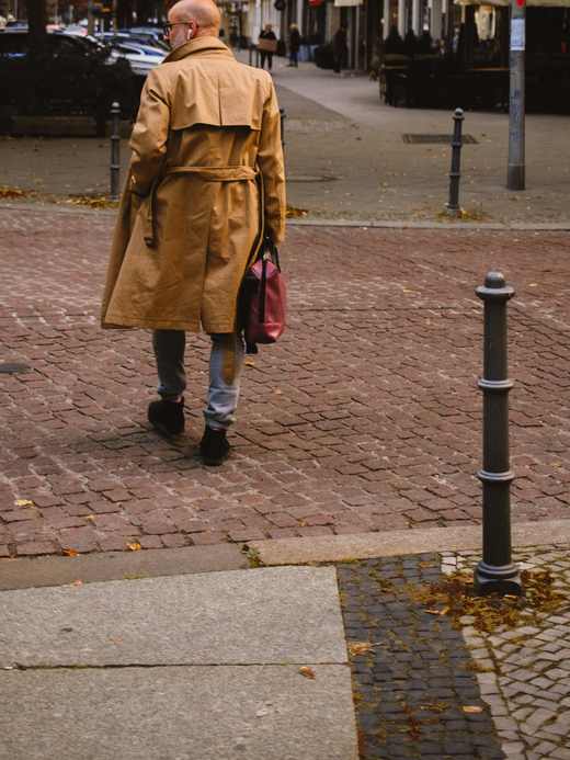 Persona de espaldas con un abrigo largo color camel, caminando por una calle de adoquines