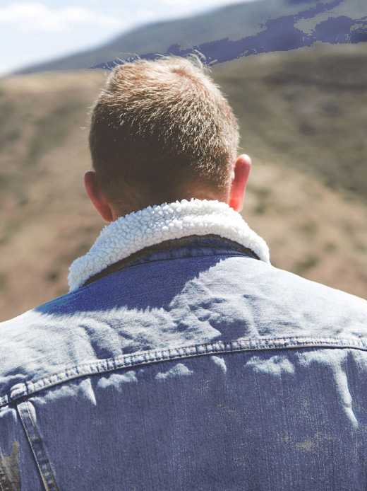 Cuello de borrego de una chaqueta de mezclilla visto desde atrás, con un cerro al fondo