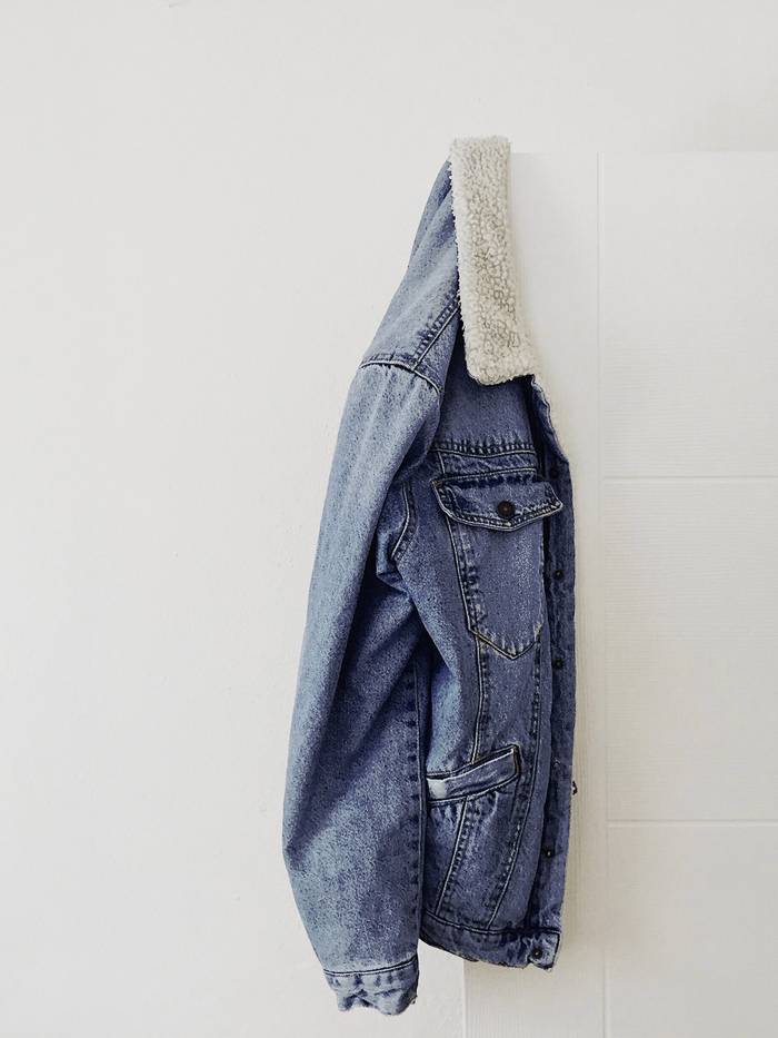 Chaqueta de mezclilla con cuello de borrego colgada de un gancho sobre una pared blanca