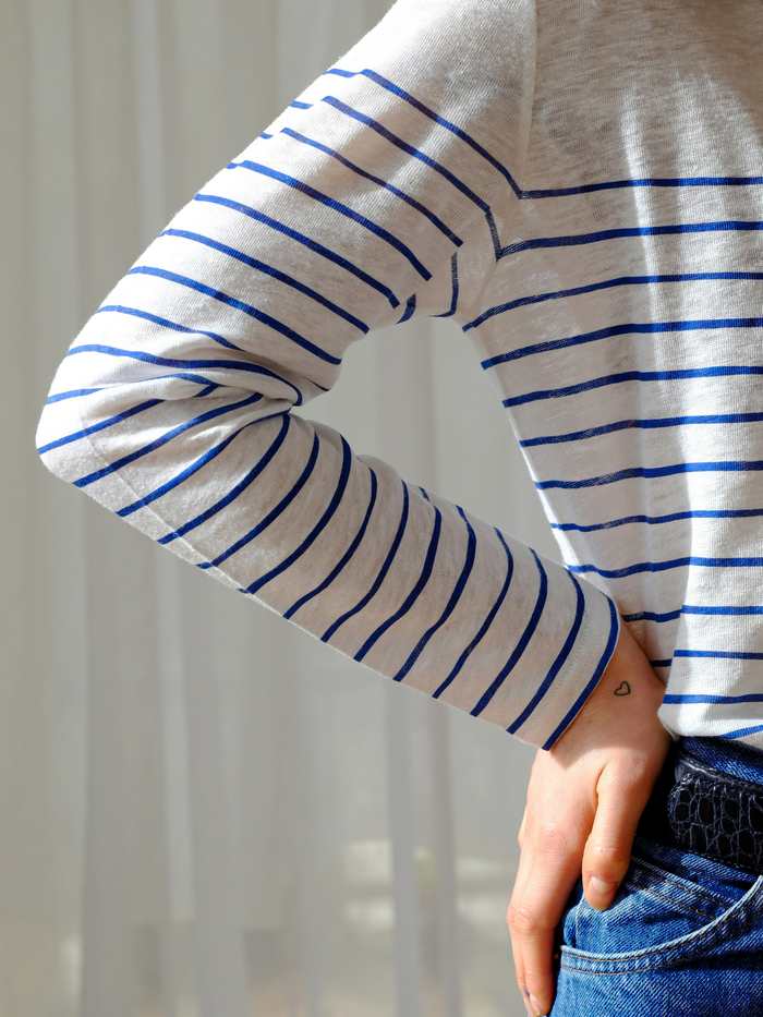 Persona de pie con la mano en el bolsillo, con una camiseta de rayas azules sobre crudo