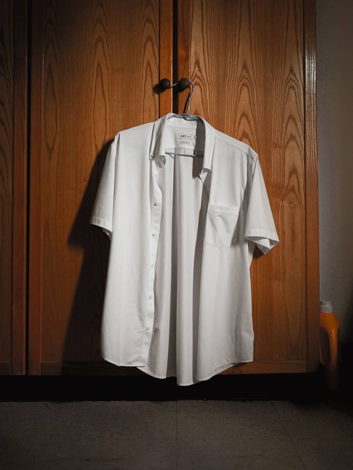 Camisa blanca de manga corta colgada frente a una puerta de madera