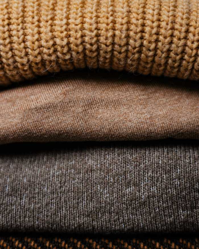 Suéteres de punto doblados en capas, en mostaza, camello y gris