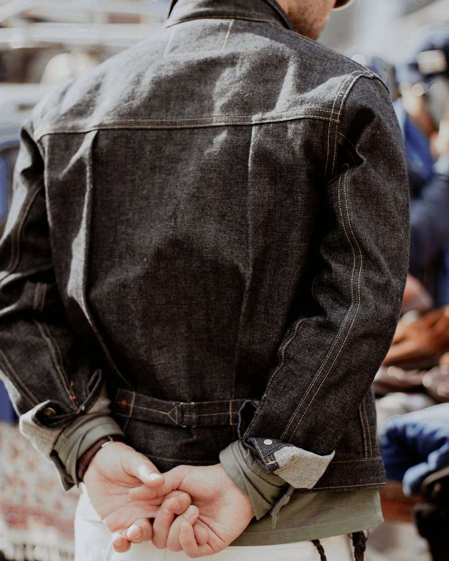 Persona de espaldas con una chaqueta de cuero oscuro y las manos cruzadas atrás