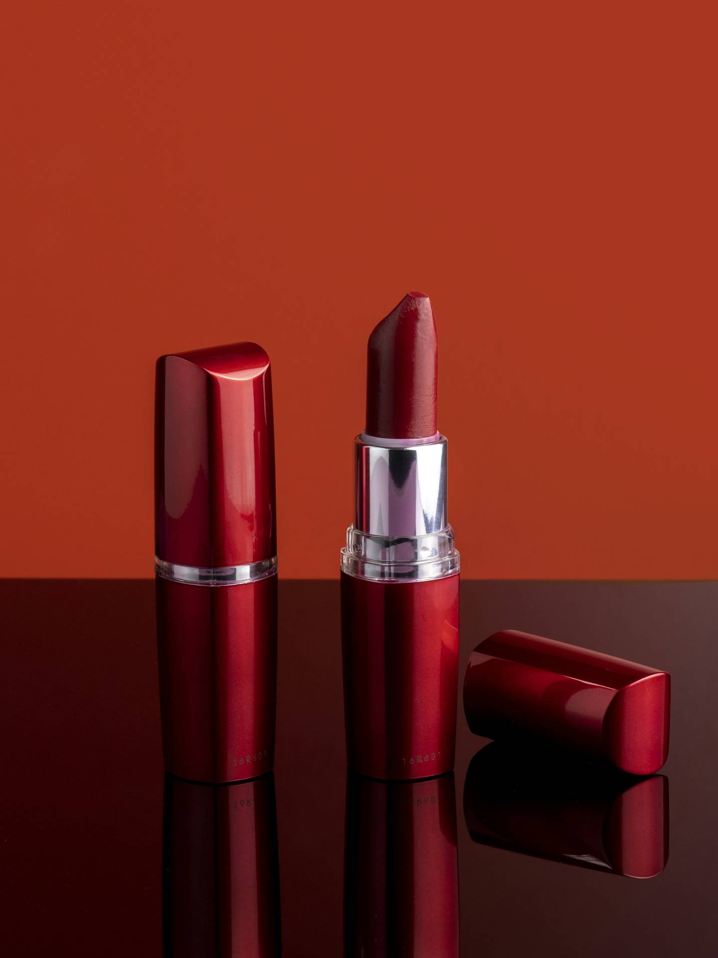 Barras de labios rojas sobre una superficie brillante frente a un fondo color ladrillo
