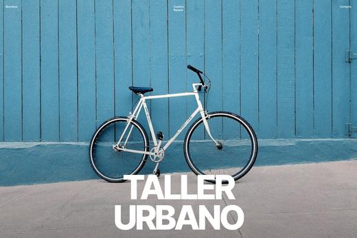 Fotografía de una bicicleta blanca apoyada en un muro azul con la palabra «Taller»