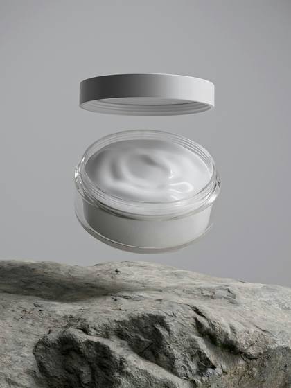 Tarro de crema abierto con su tapa suspendida sobre una roca gris