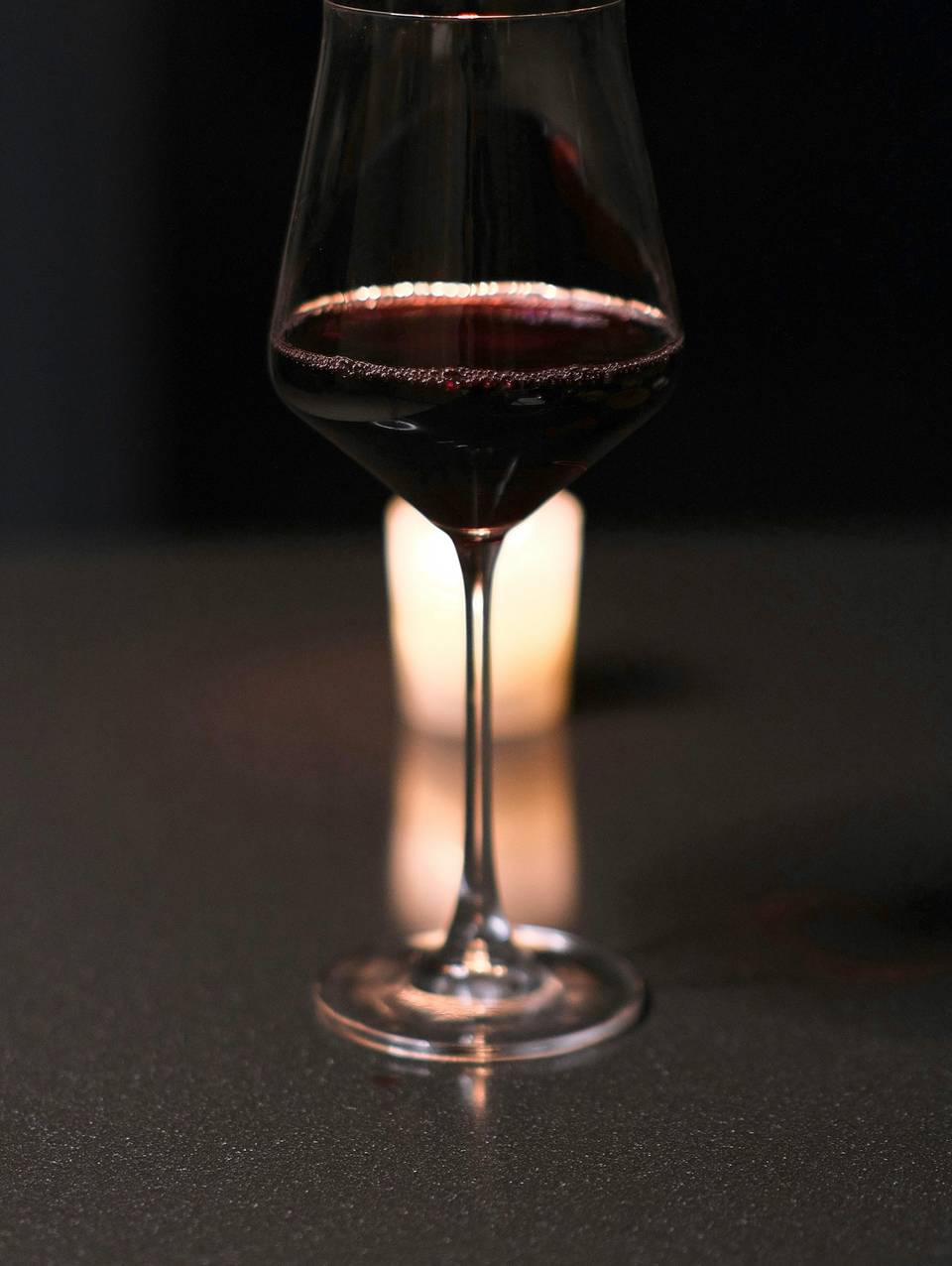 Copa de vino tinto sobre una barra oscura, con una vela encendida detrás