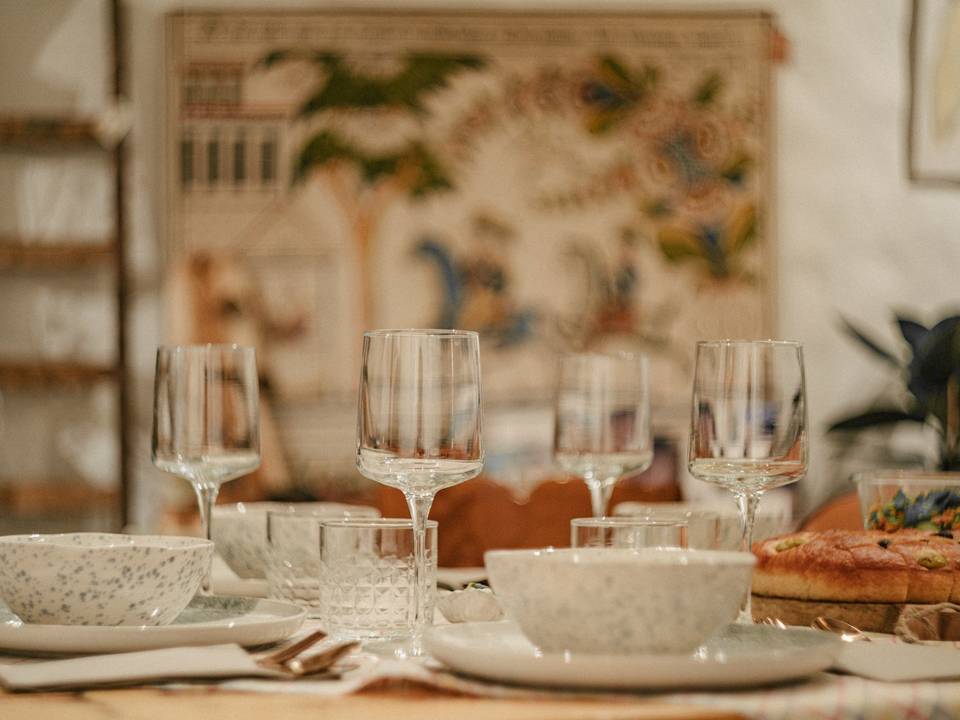 Mesa servida con copas, cuencos y platos junto a una pared con tapiz