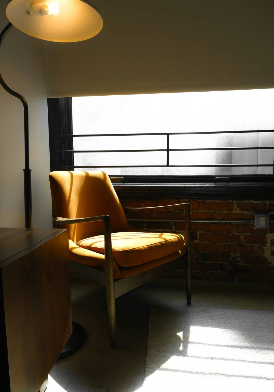 Sillón de cuero ocre junto a una ventana, con una lámpara sobre él
