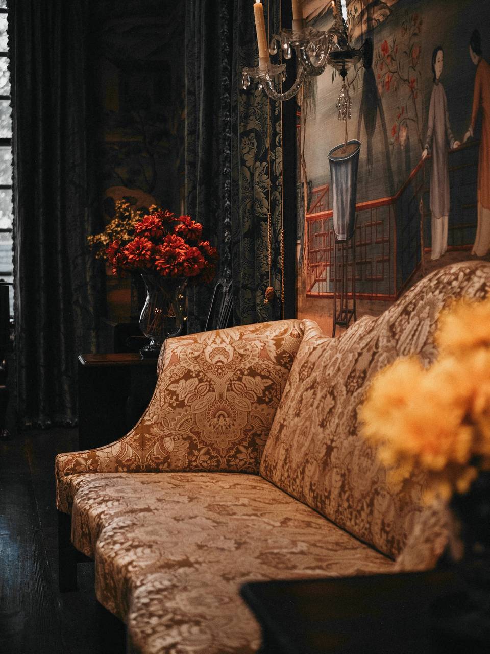 Sofá de tela estampada junto a una cortina oscura y flores naranjas