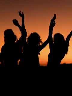 Tres siluetas con los brazos en alto al atardecer