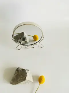 Espejo redondo con soporte, una piedra y una flor amarilla