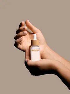 Mano sosteniendo un frasco con gotero sobre fondo beige