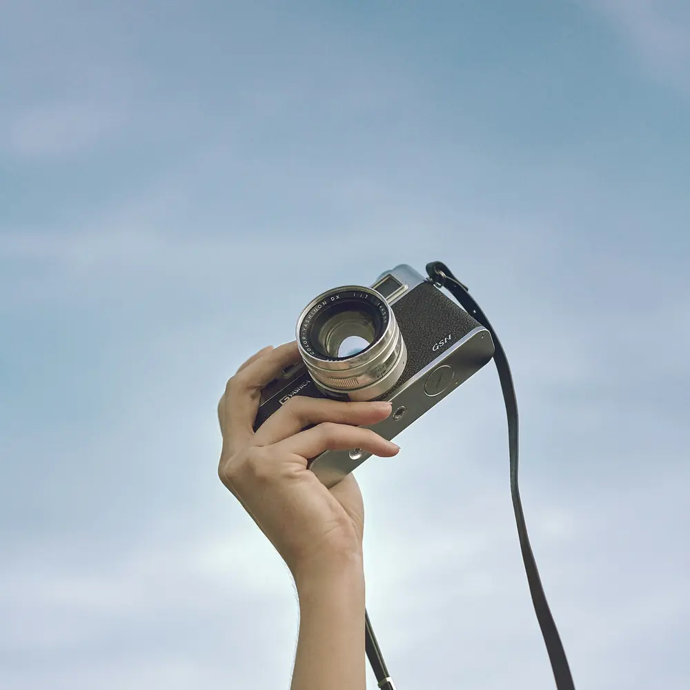 Mano en alto sosteniendo una cámara de fotos contra el cielo