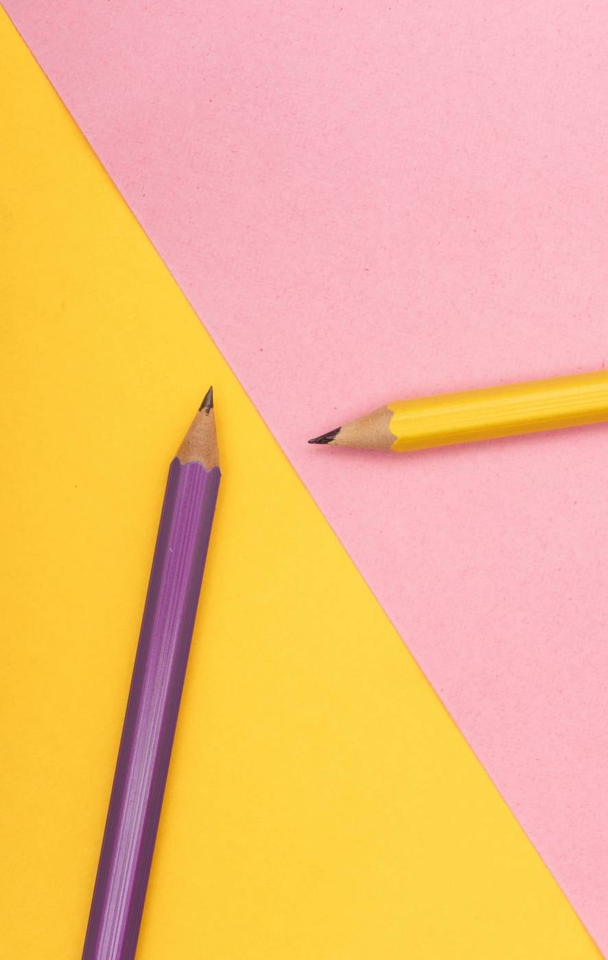 Lápiz violeta y lápiz amarillo sobre papeles rosado y amarillo