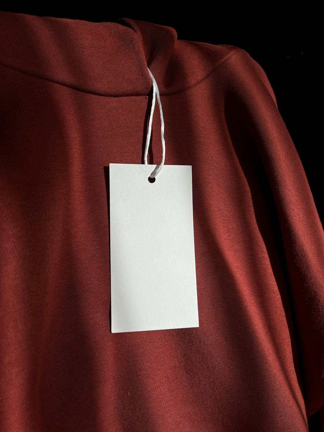 Etiqueta blanca colgando de un buzo rojo oscuro