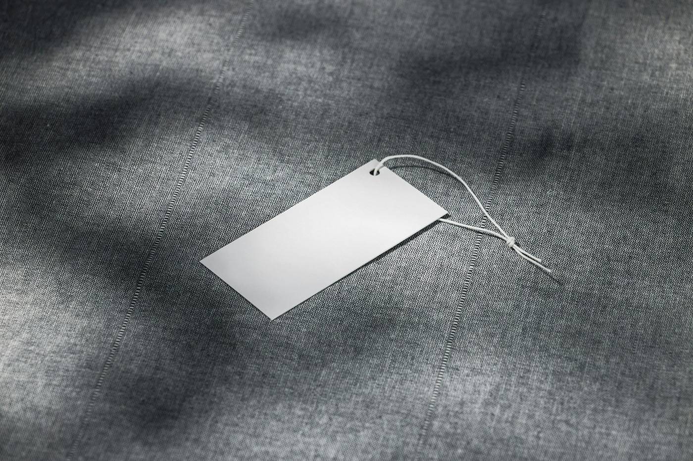 Etiqueta de cartón blanca con cordel sobre una tela gris