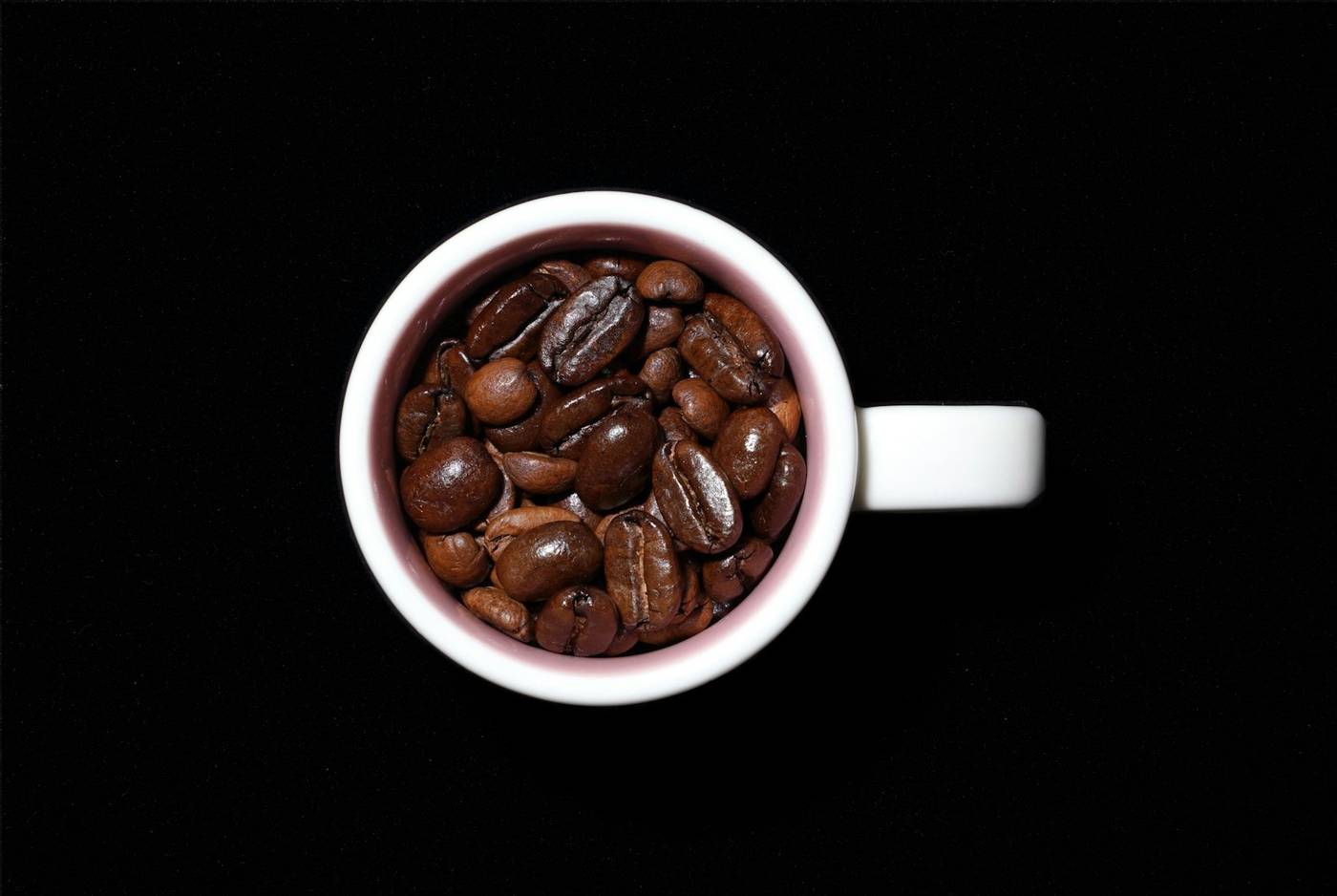 Taza blanca llena de granos de café sobre un fondo negro