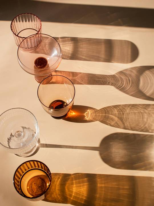 Vasos de vidrio ámbar y sus sombras largas sobre una mesa clara