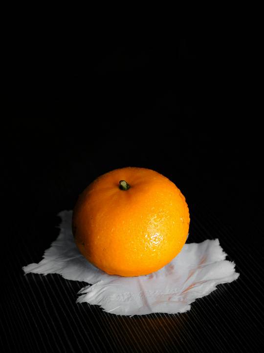Una naranja sobre un papel blanco arrugado, con fondo negro