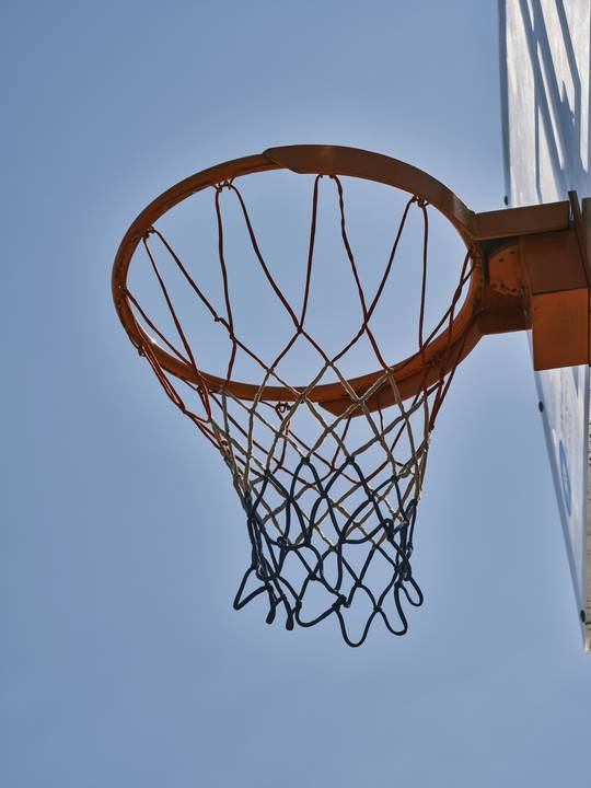 Aro de básquetbol con red visto desde abajo contra un cielo azul claro