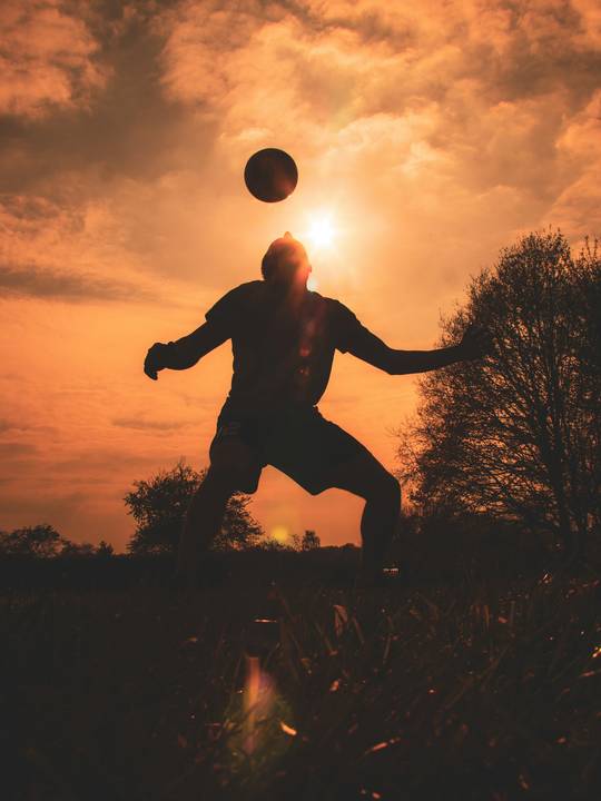 Silueta de una persona jugando con una pelota al atardecer, contra el sol