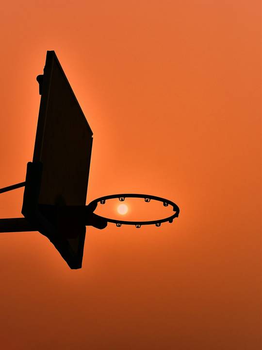 Tablero y aro de básquetbol a contraluz sobre un cielo naranja