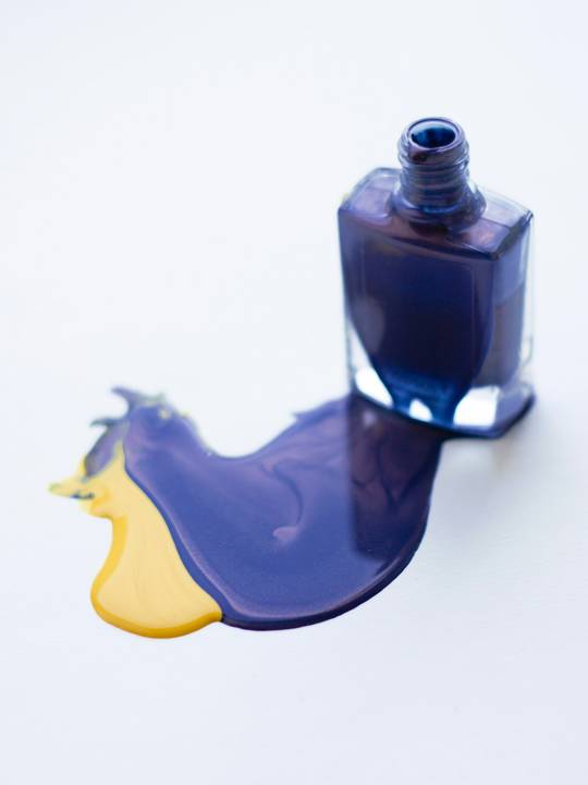 Frasco de esmalte azul derramado sobre un fondo blanco