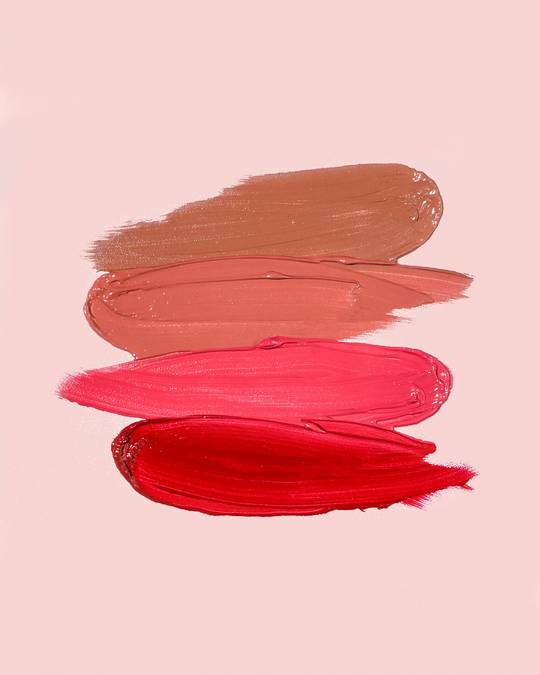 Trazos de labial en tonos rosados y rojos sobre un fondo rosa