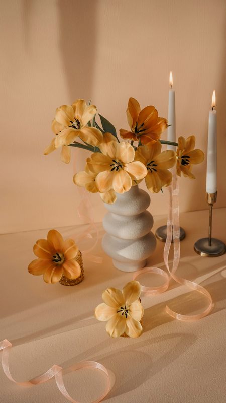 Flores amarillas en un jarrón de cerámica, con dos velas encendidas y cintas claras