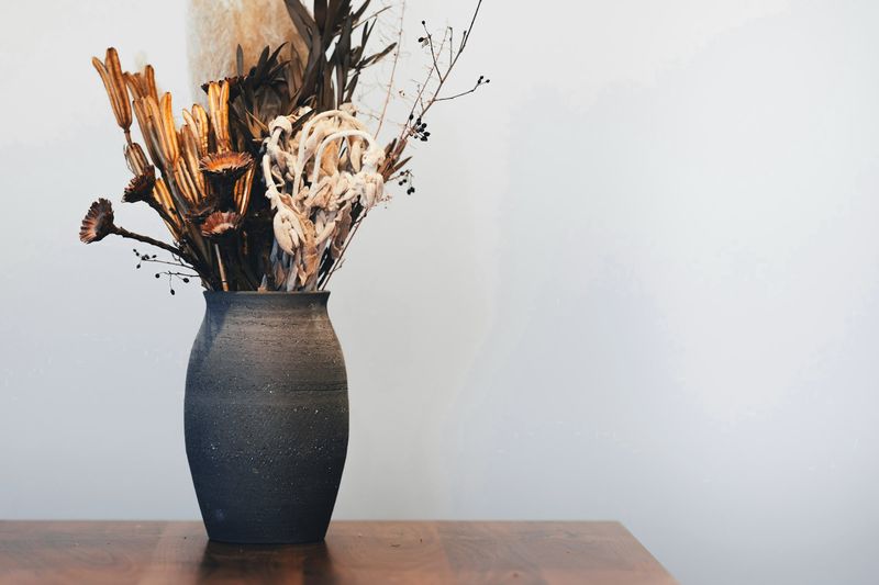 Jarrón de barro oscuro con flores secas sobre una mesa de madera