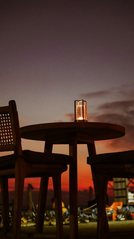 Mesa redonda con un farol encendido y sillas de rejilla contra un cielo de ocaso